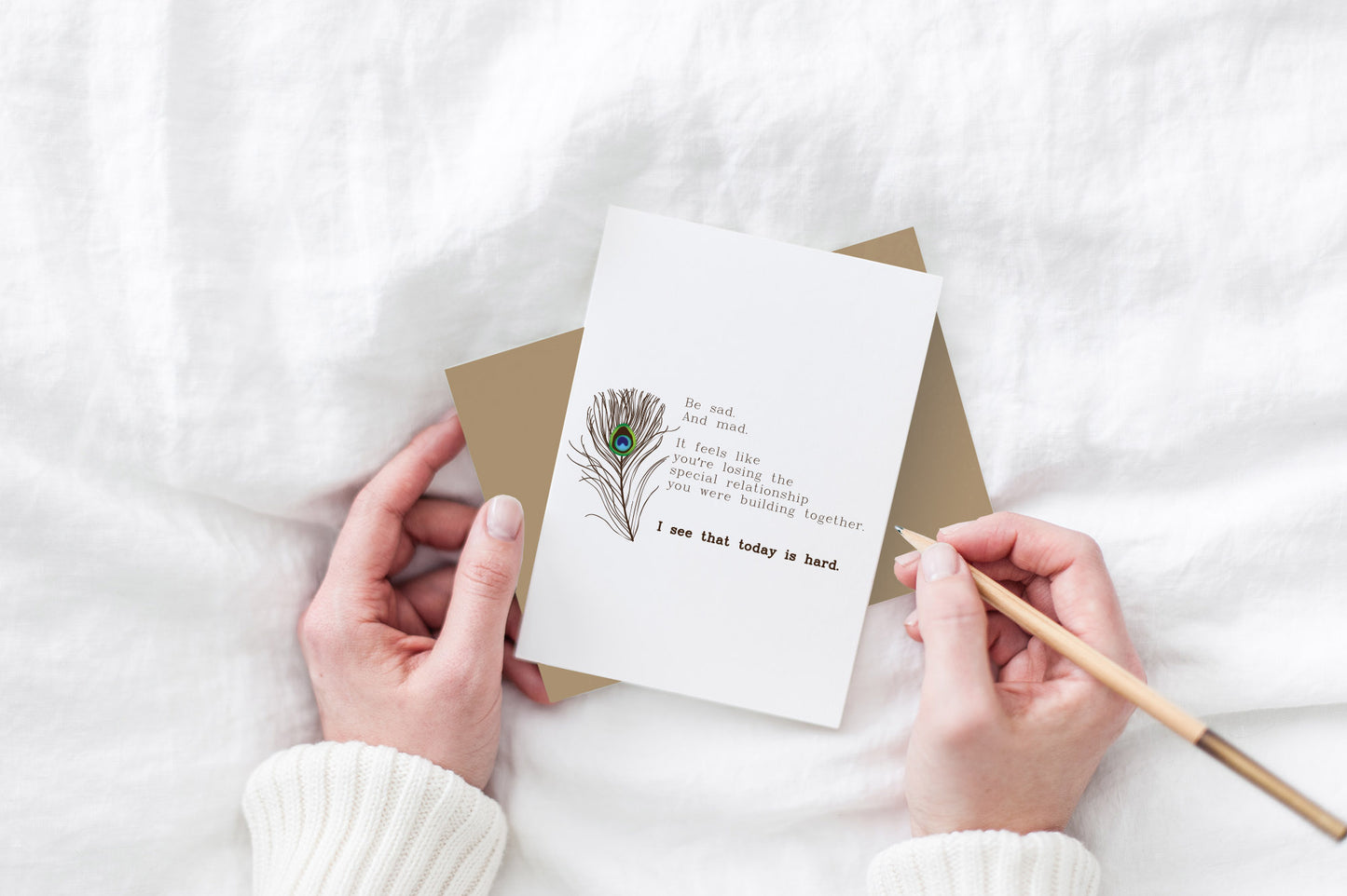 Greeting card, seen from above, with a kraft, square flap envelope, pencils, pencil sharpener and shavings on a white background.