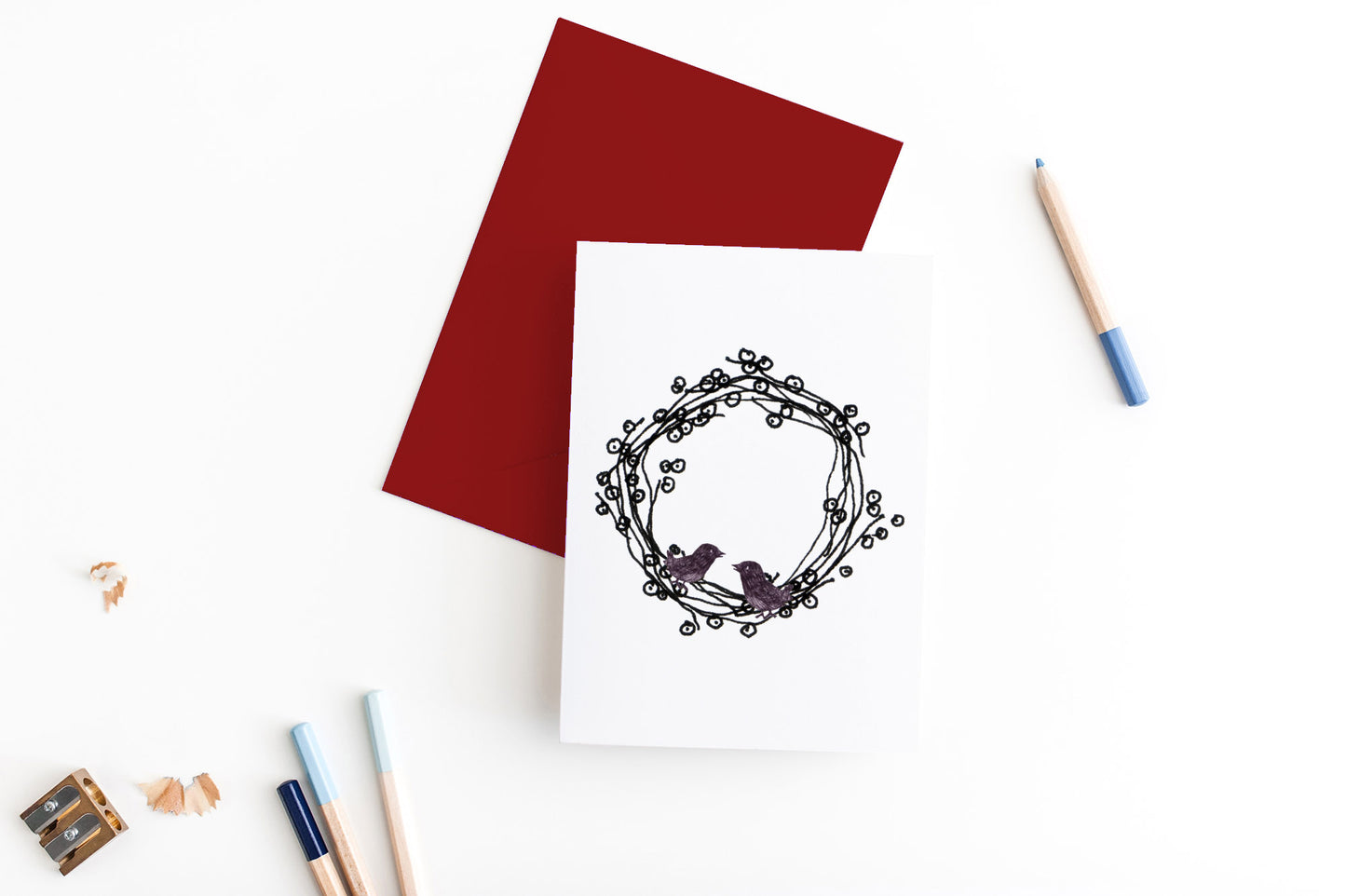 Greeting card, seen from above, with a colored, square flap envelope, pencils, pencil sharpener and shavings on a white background.