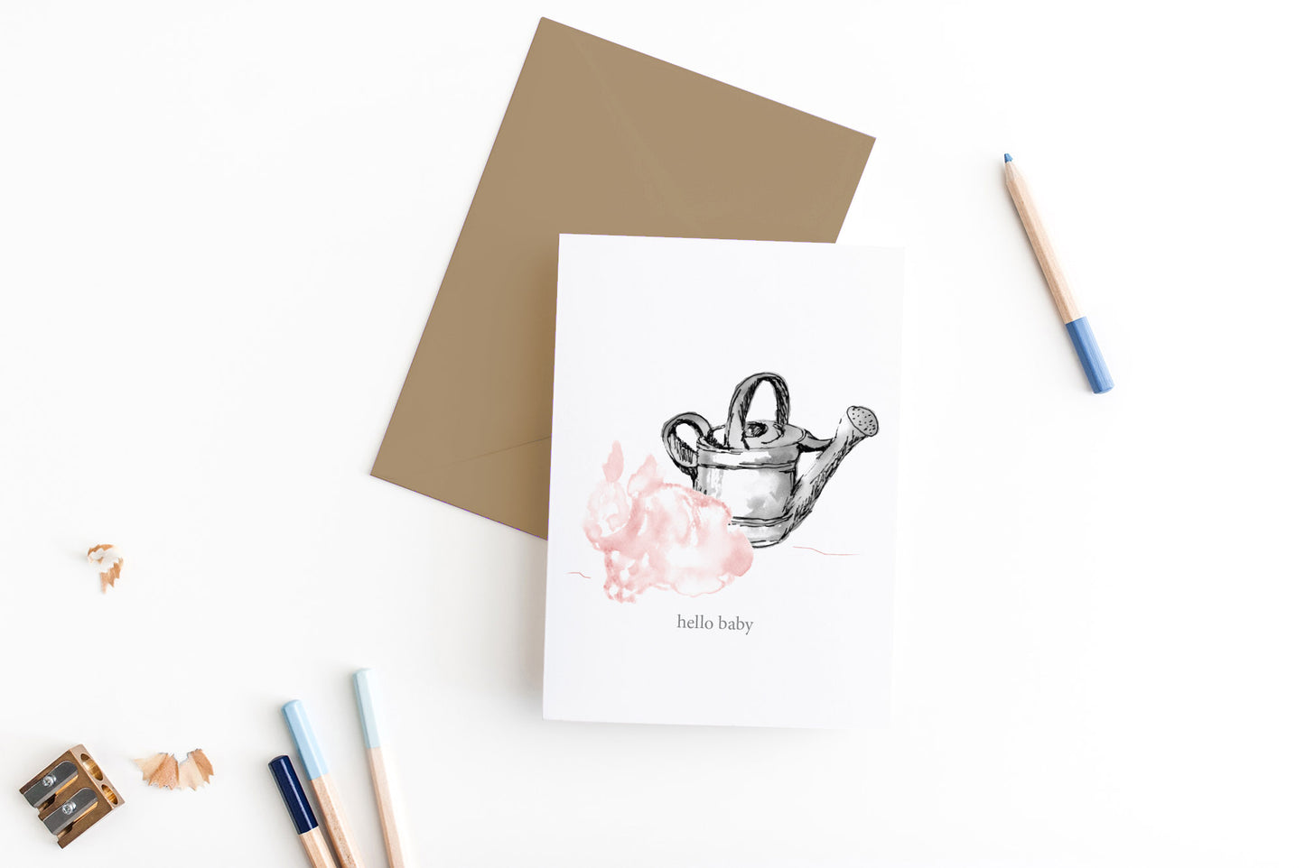 Greeting card, seen from above, with a colored, square flap envelope, pencils, pencil sharpener and shavings on a white background.