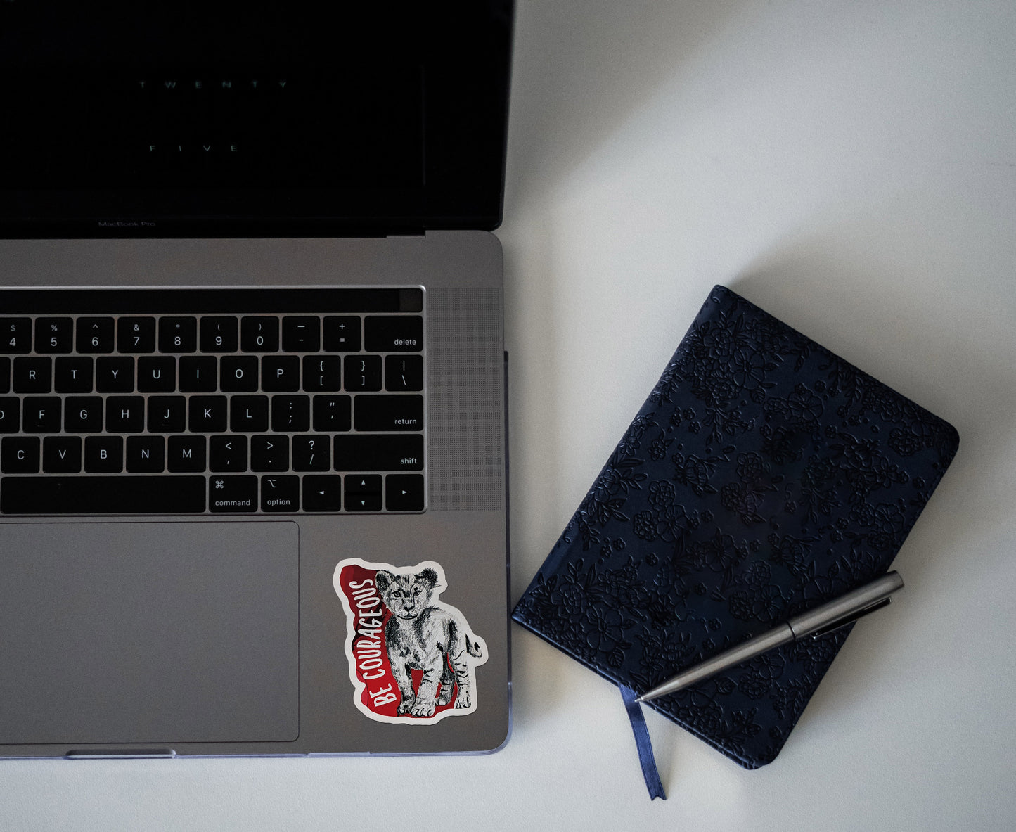Digital mockup of a sticker on the bottom left corner of a laptop keyboard next to a notebook.