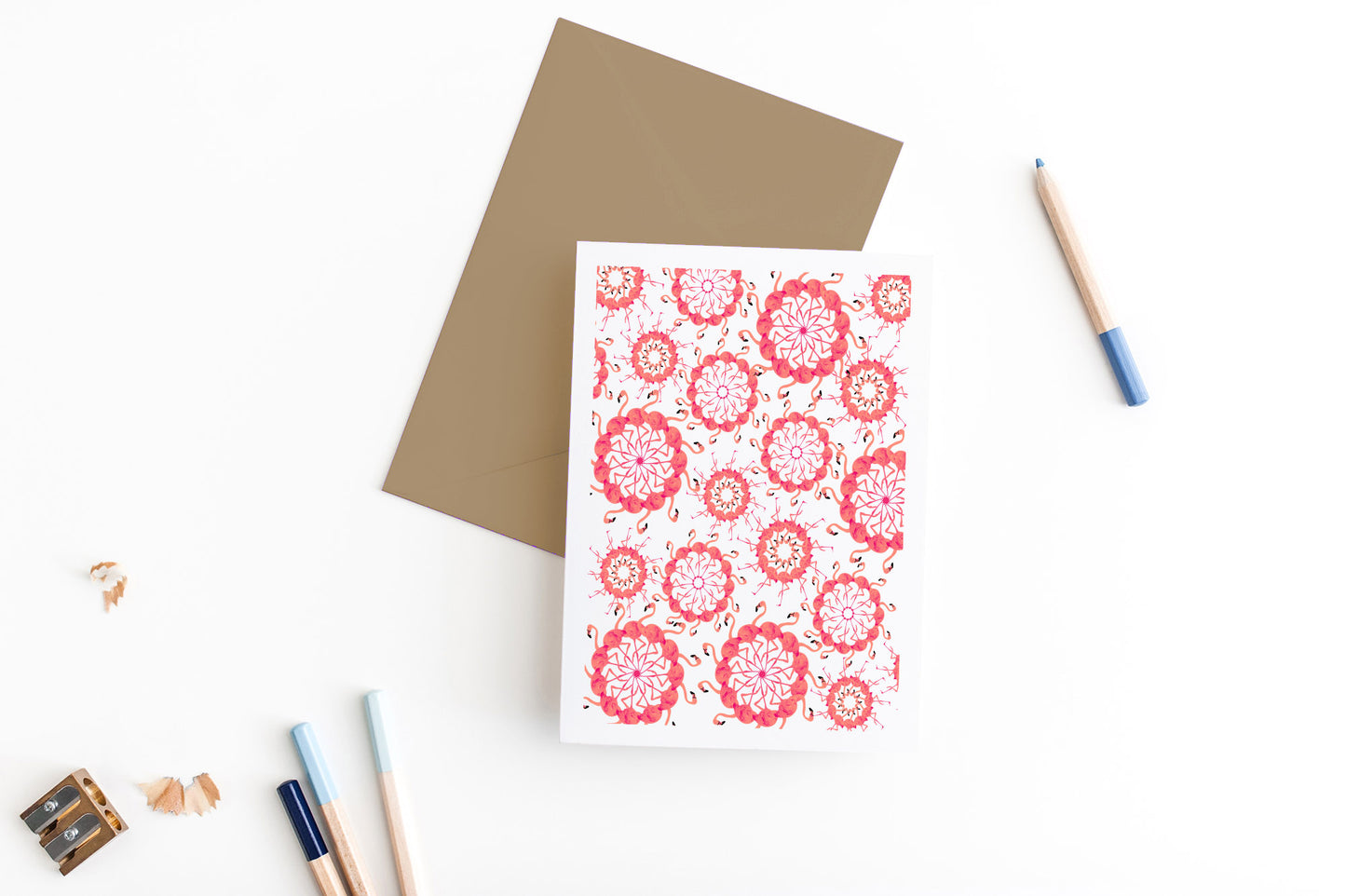 Greeting card, seen from above, with a kraft, square flap envelope, pencils, pencil sharpener and shavings on a white background.