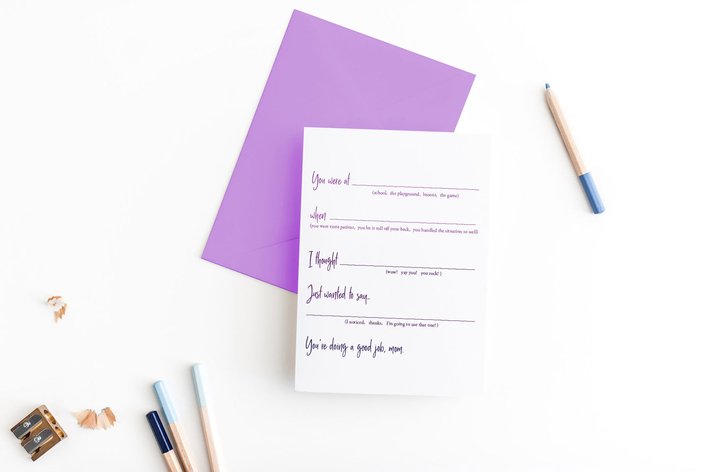 Greeting card, seen from above, with a colored, square flap envelope, pencils, pencil sharpener and shavings on a white background.