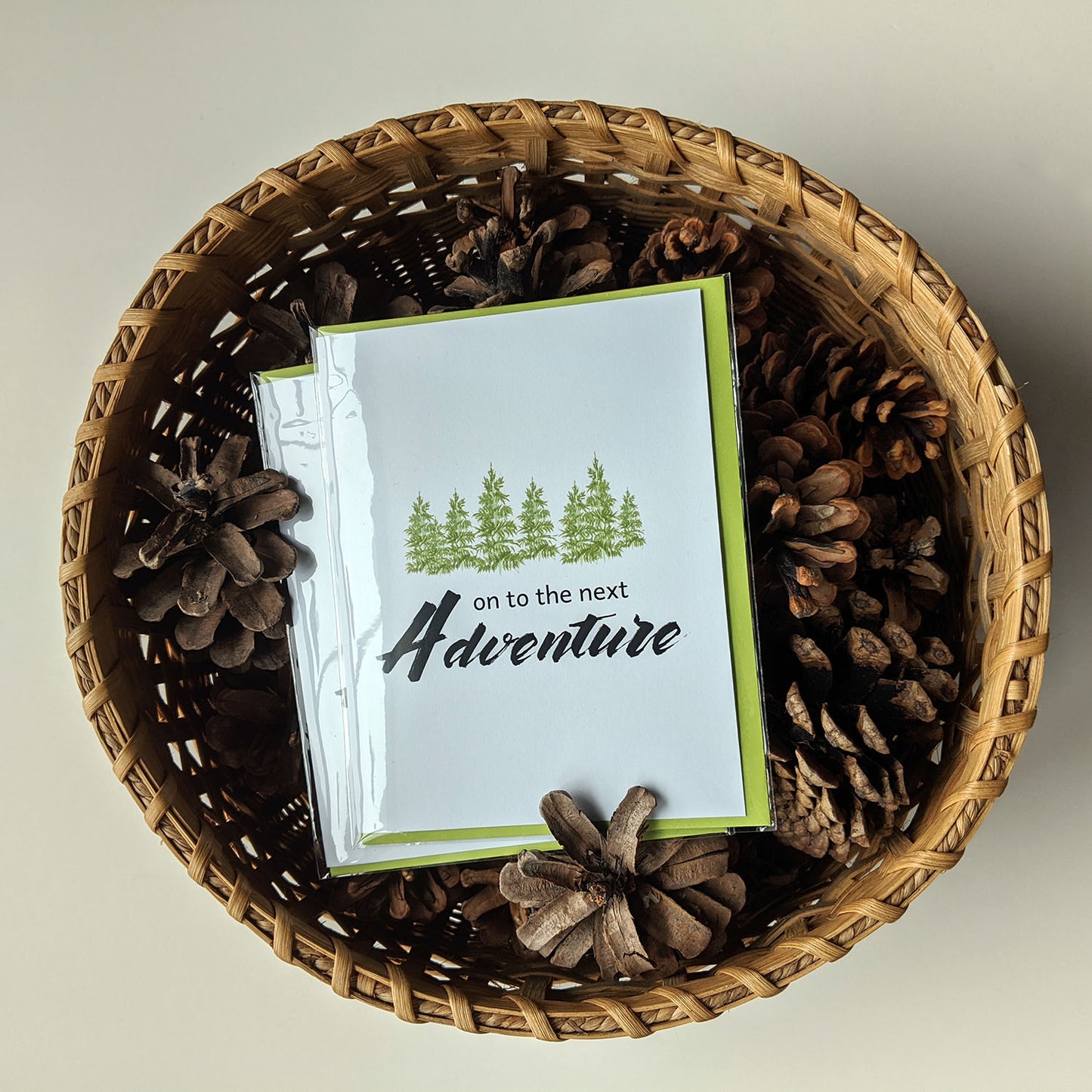 Greeting card laying on pinecones in a woven basket.