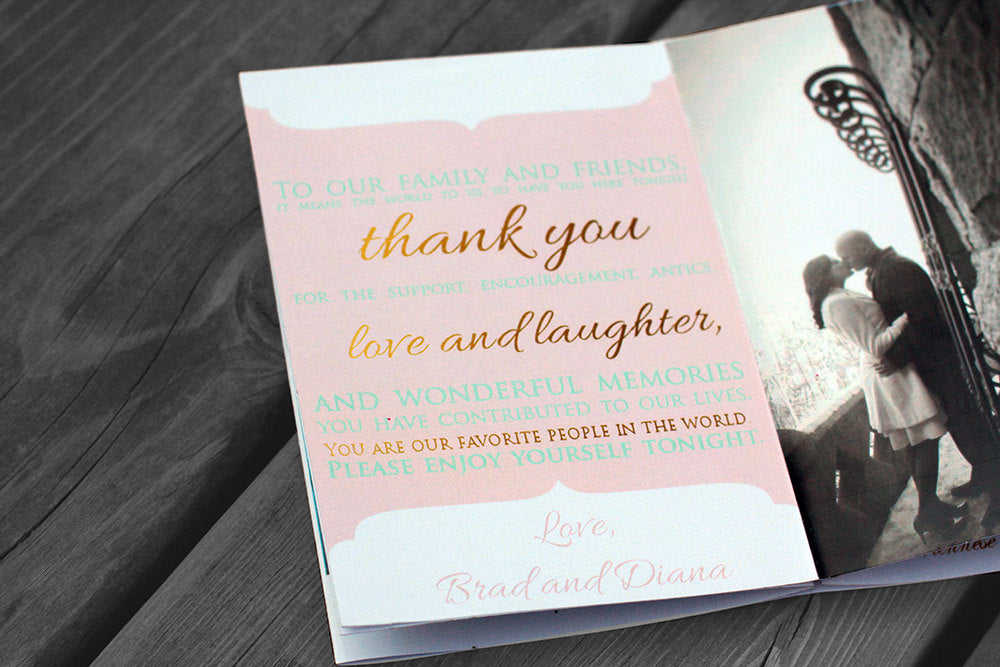 Centerpiece laying flat on wooden boards showing the thank you note from the couple to the guests and part of an engagement photo kissing along a stone balcony.