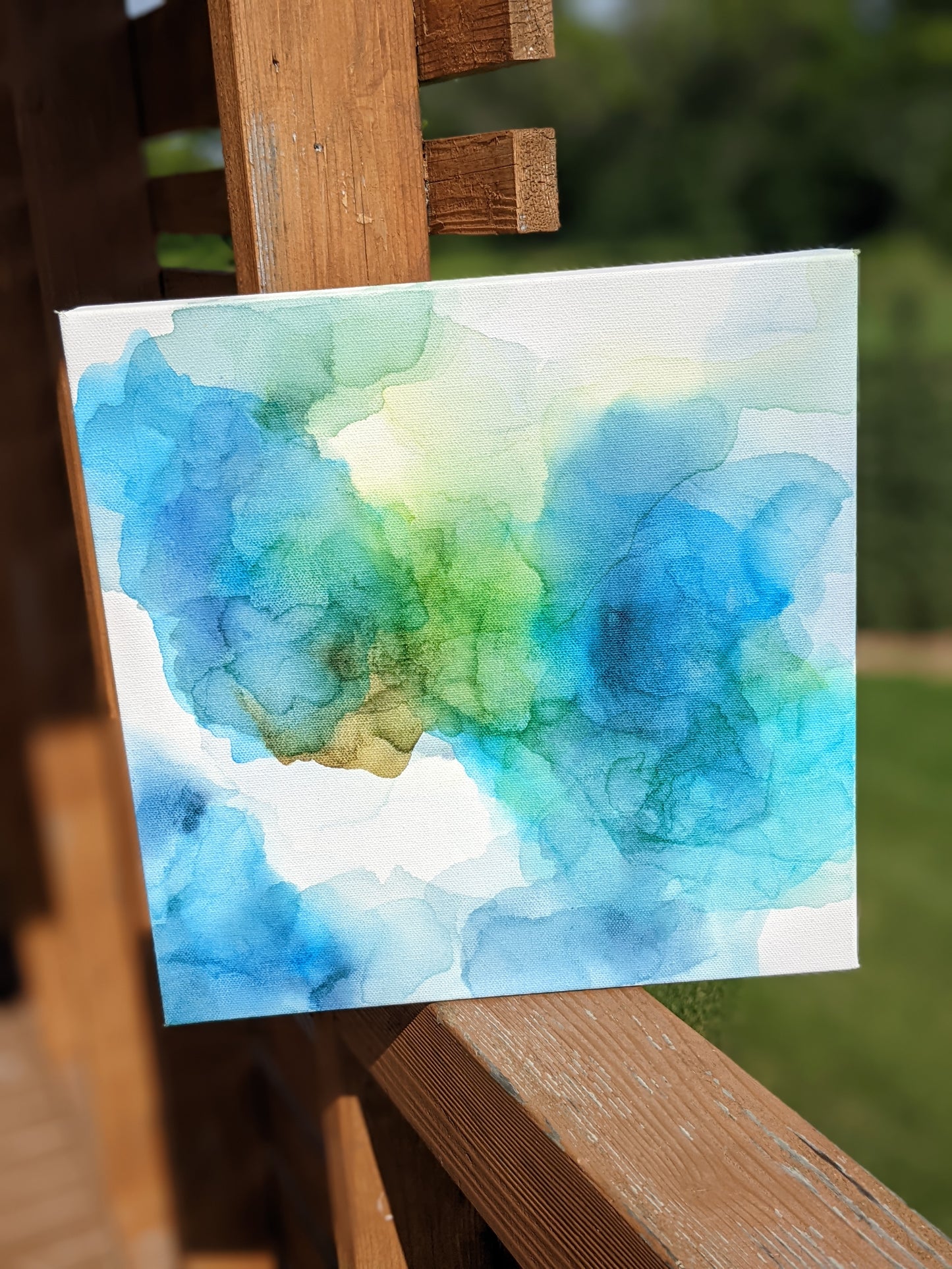 Canvas shown outdoors sitting on a wooden railing with greenery in the background.