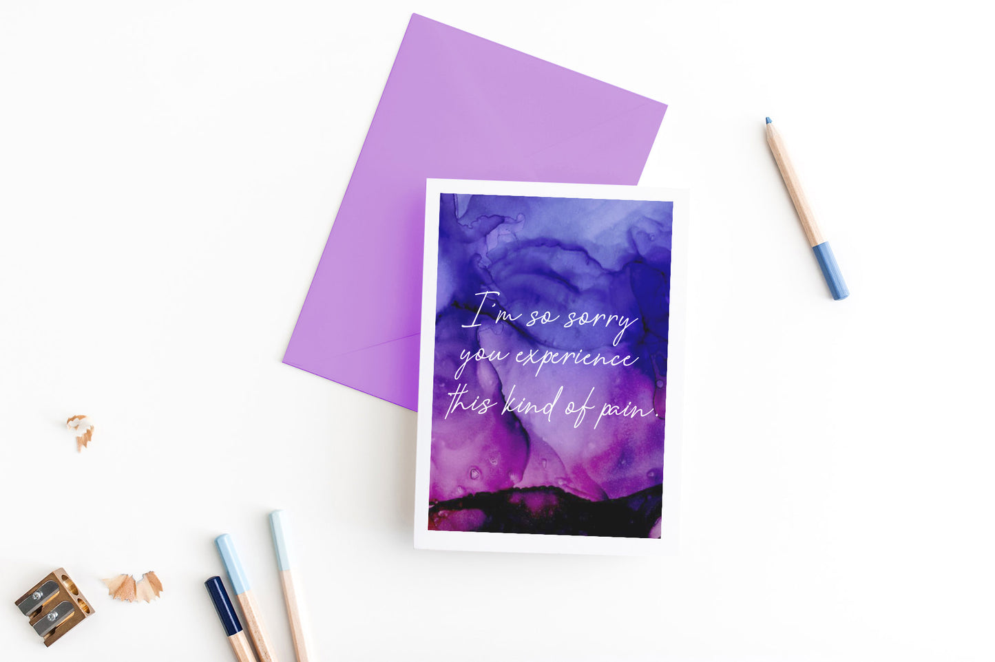 Greeting card, seen from above, with a colored, square flap envelope, pencils, pencil sharpener and shavings on a white background.
