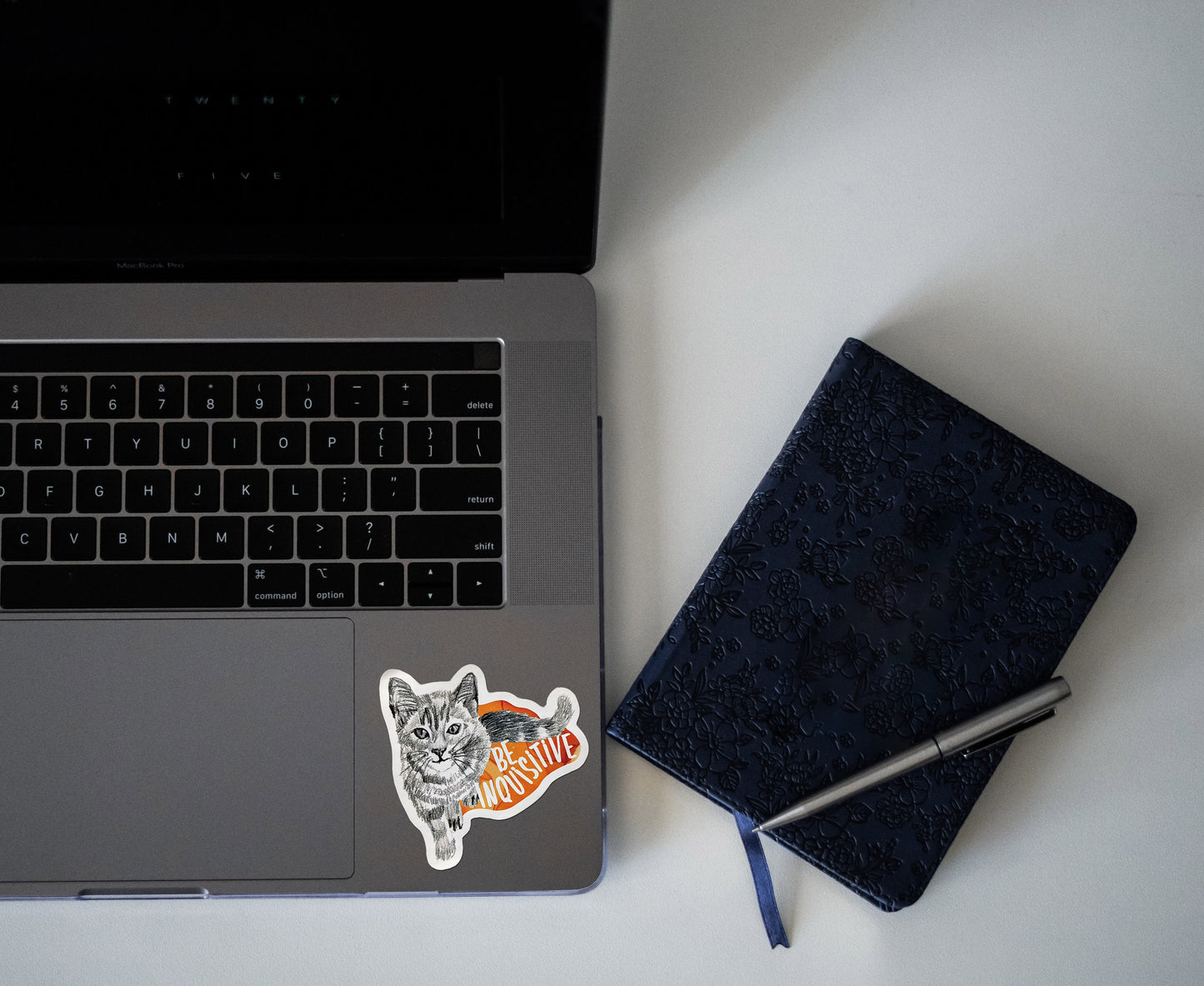 Digital mockup of a sticker on the bottom left corner of a laptop keyboard next to a notebook.