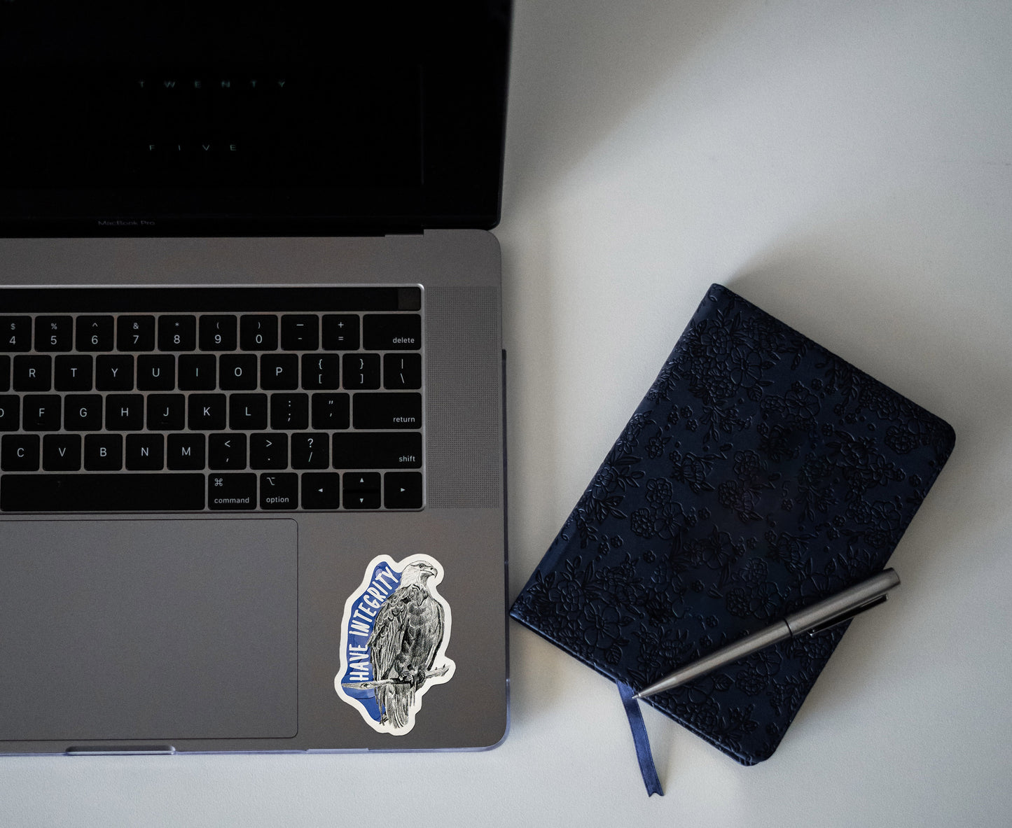 Digital mockup of a sticker on the bottom left corner of a laptop keyboard next to a notebook.