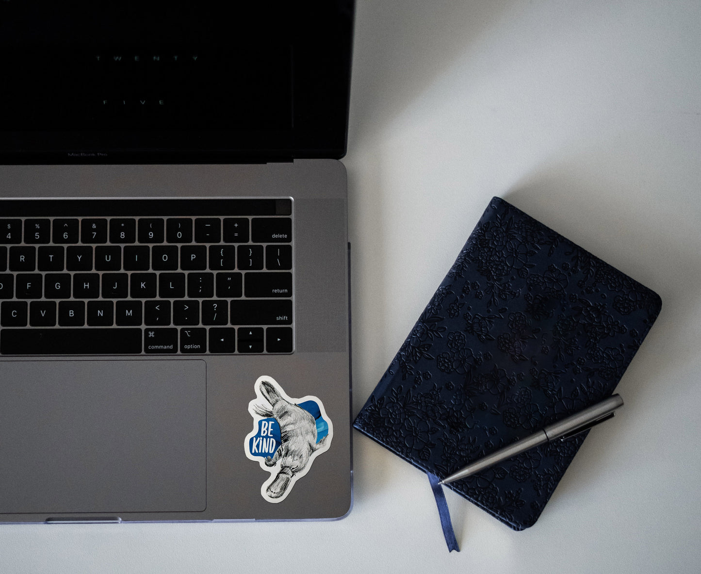 Digital mockup of a sticker on the bottom left corner of a laptop keyboard next to a notebook.
