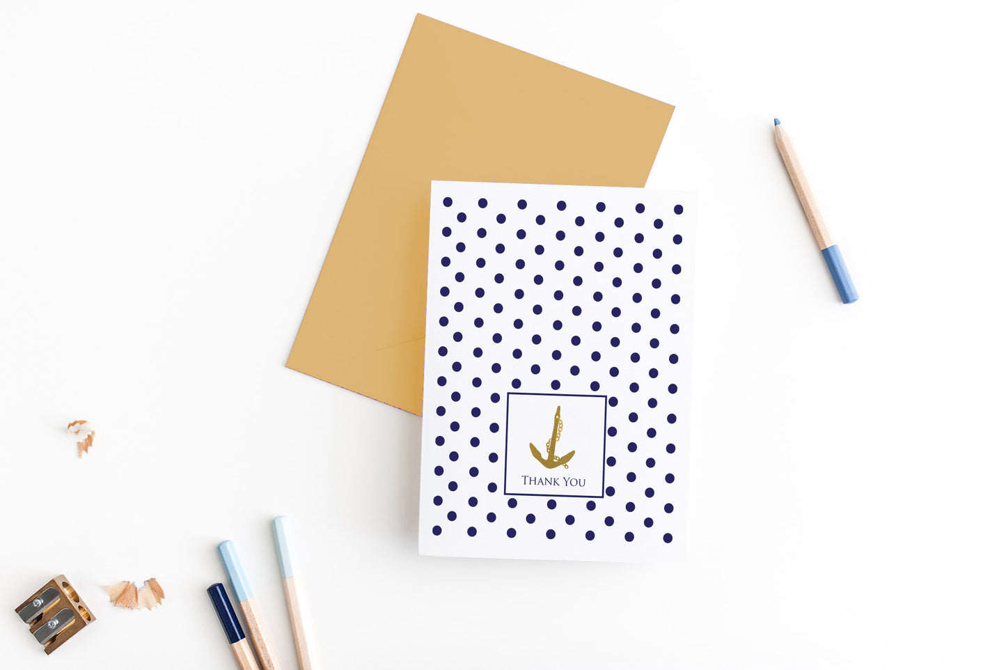 Greeting card, seen from above, with a colored, square flap envelope, pencils, pencil sharpener and shavings on a white background.