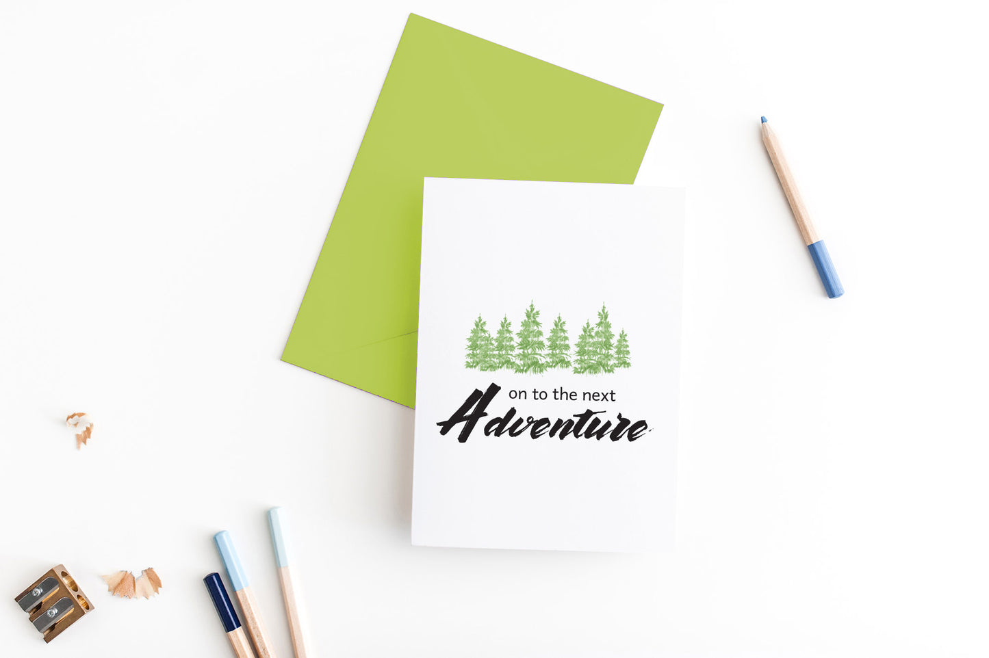Greeting card, seen from above, with a colored, square flap envelope, pencils, pencil sharpener and shavings on a white background.