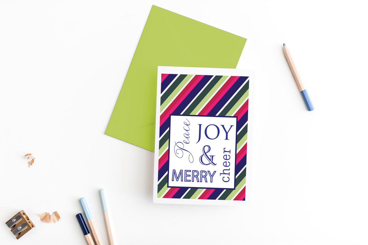 Greeting card, seen from above, with a colored, square flap envelope, pencils, pencil sharpener and shavings on a white background.