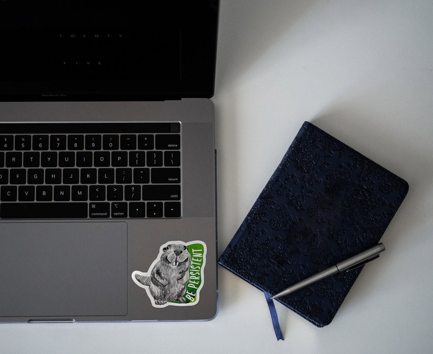 Digital mockup of a sticker on the bottom left corner of a laptop keyboard next to a notebook.