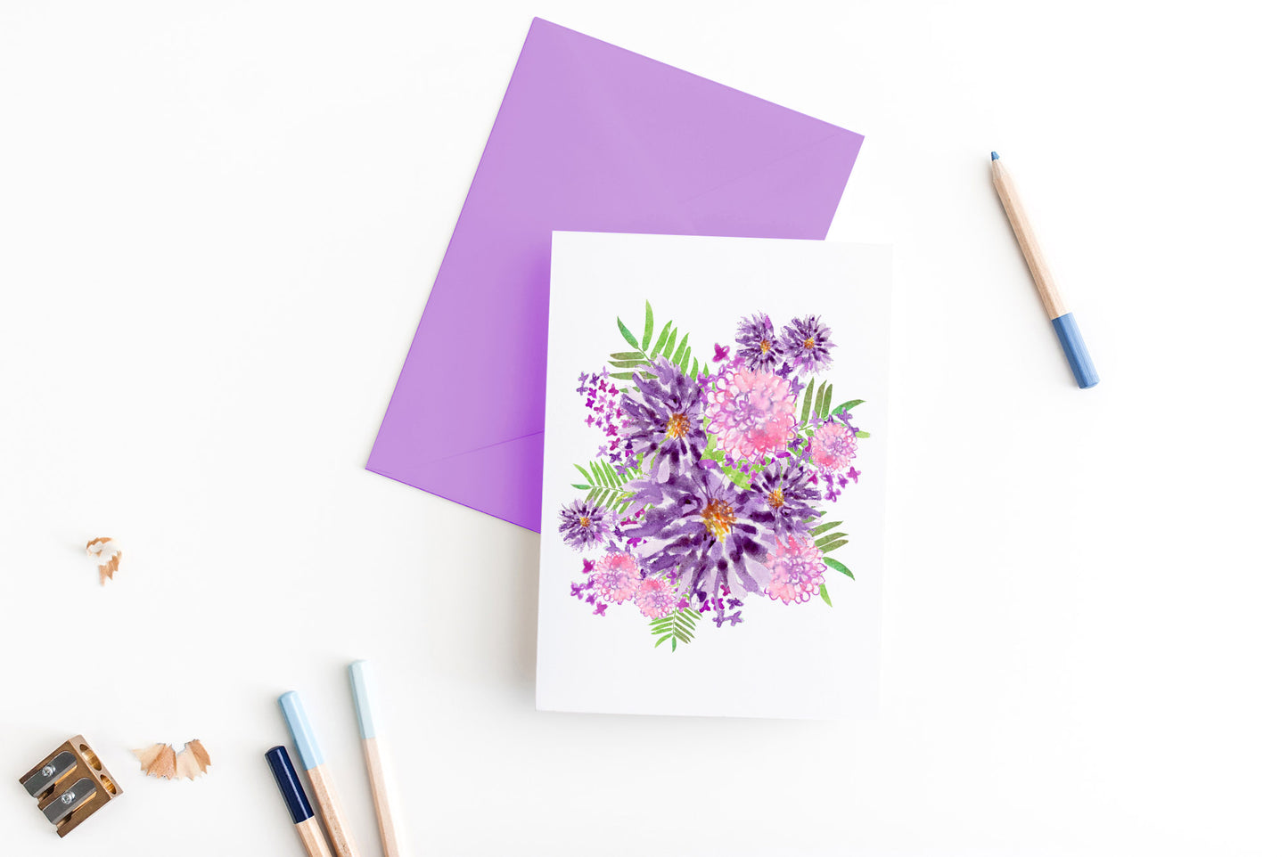 Greeting card, seen from above, with a colored, square flap envelope, pencils, pencil sharpener and shavings on a white background.