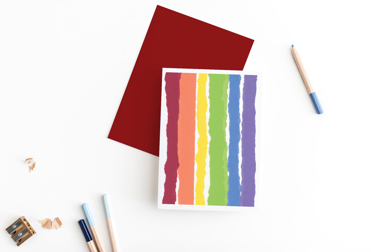 Greeting card, seen from above, with a colored, square flap envelope, pencils, pencil sharpener and shavings on a white background.