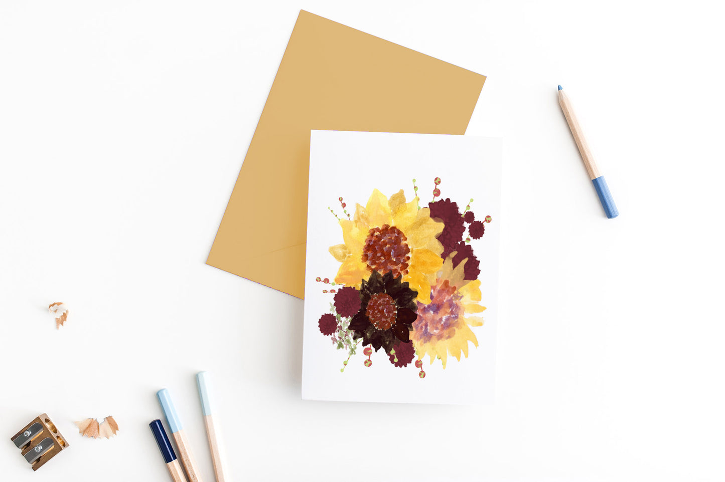 Greeting card, seen from above, with a colored, square flap envelope, pencils, pencil sharpener and shavings on a white background.