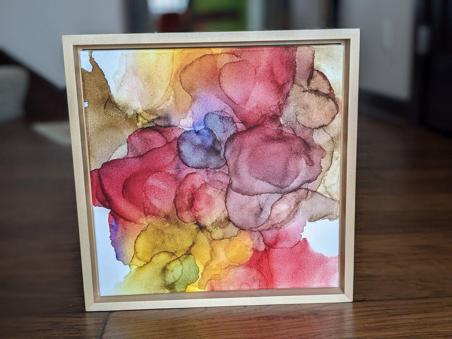 Front view of Abundance standing on a wood floor in a hallway set in a light maple float frame.