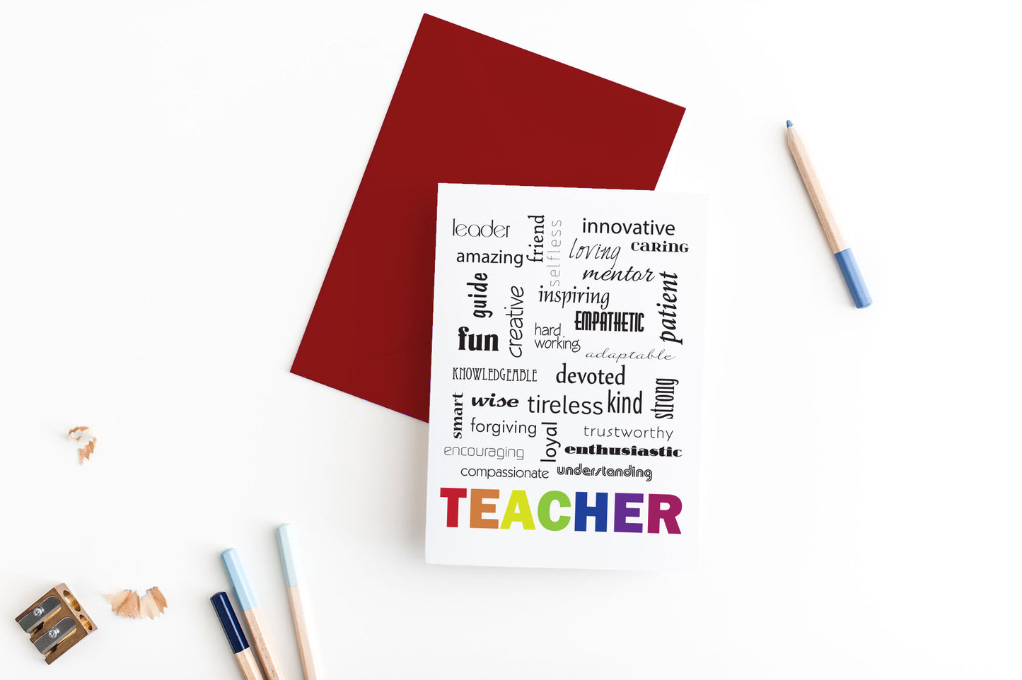 Greeting card, seen from above, with a colored, square flap envelope, pencils, pencil sharpener and shavings on a white background.