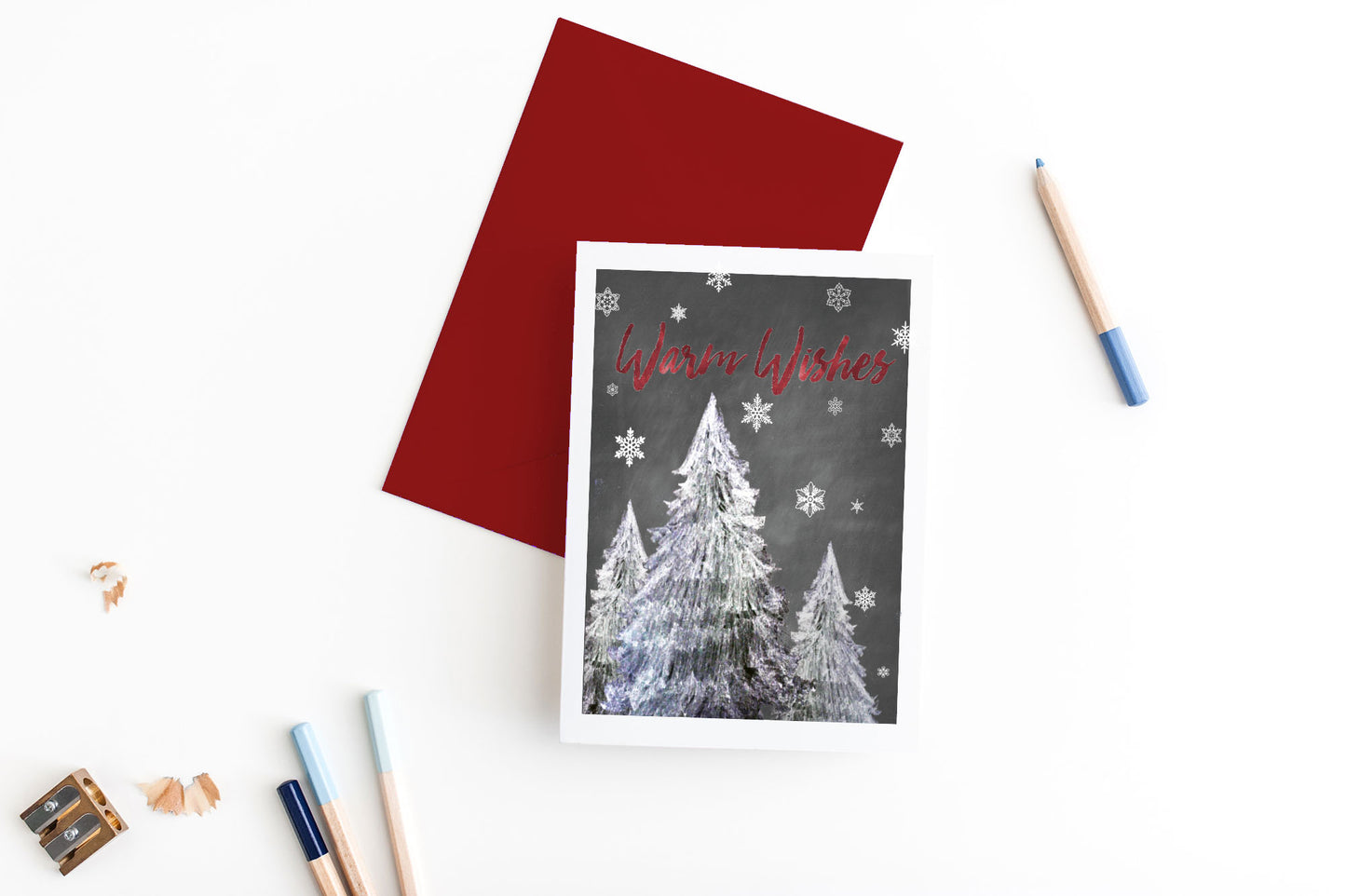 Greeting card, seen from above, with a colored, square flap envelope, pencils, pencil sharpener and shavings on a white background.