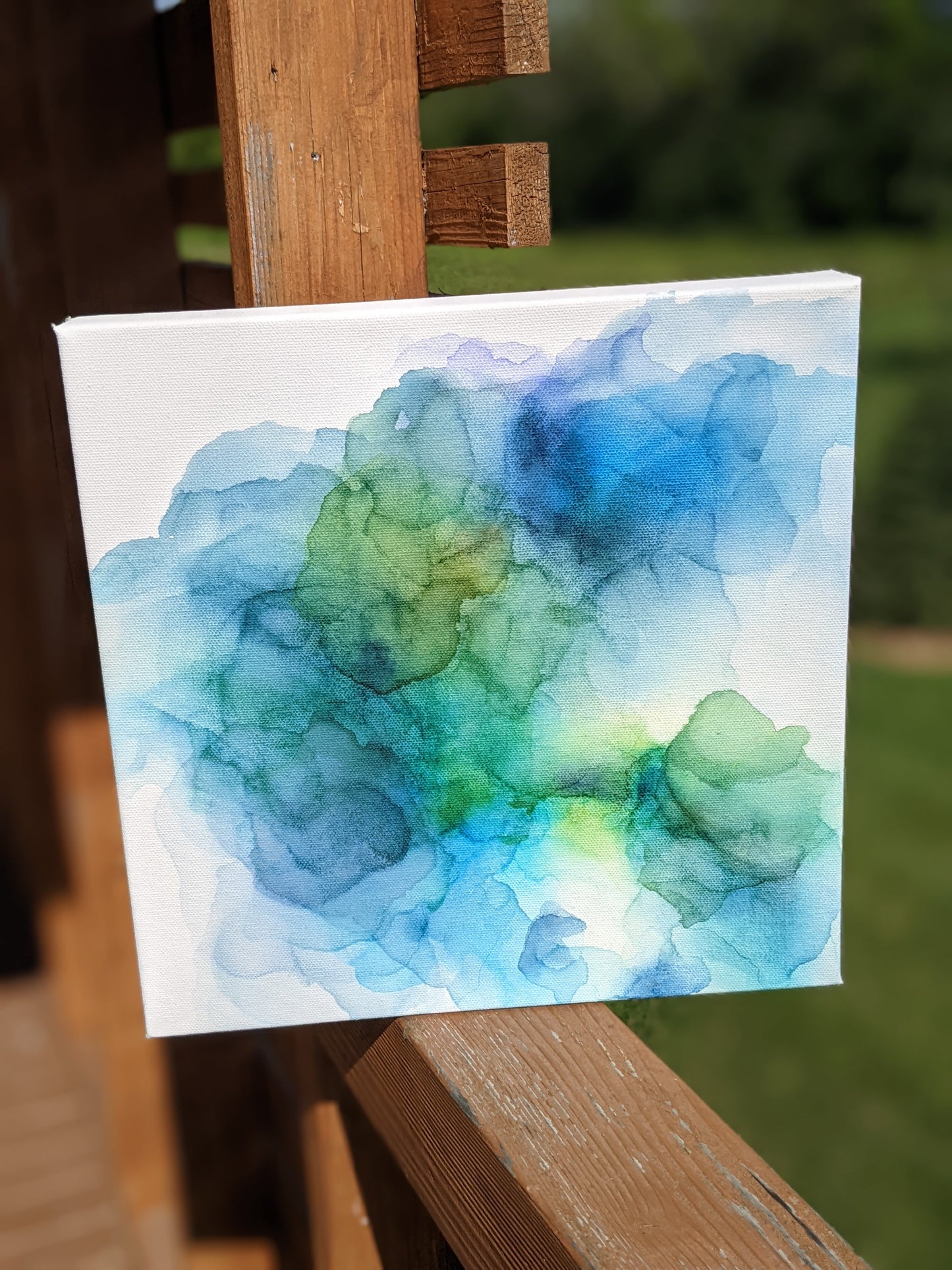 Canvas shown outdoors sitting on a wooden railing with greenery in the background.