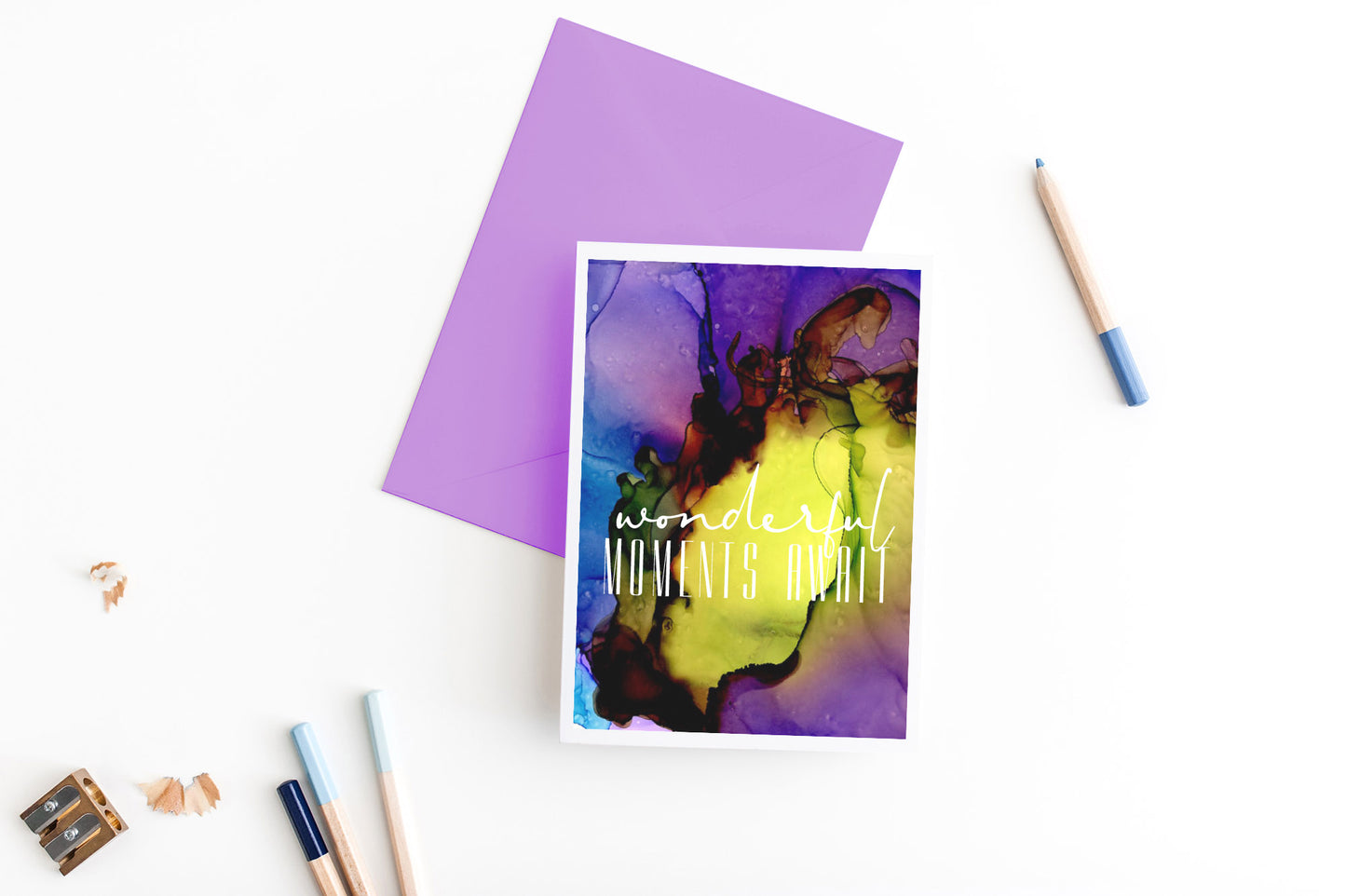 Greeting card, seen from above, with a colored, square flap envelope, pencils, pencil sharpener and shavings on a white background.