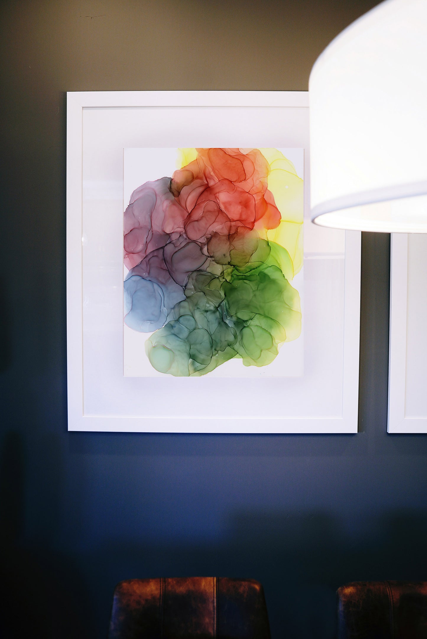 Digital mockup showing Release All Resistance framed in white hung against a deep blue wall behind a modern light fixture with leather stools below.