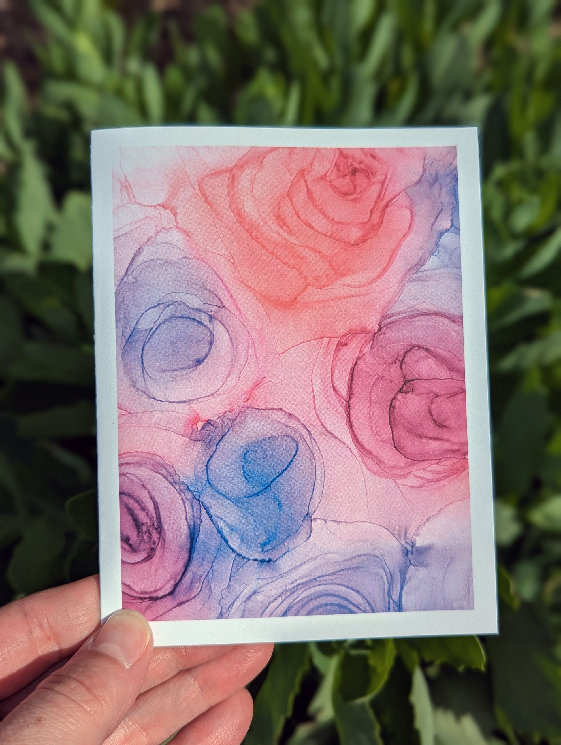 Hand holding a greeting card with green leaves in the background.