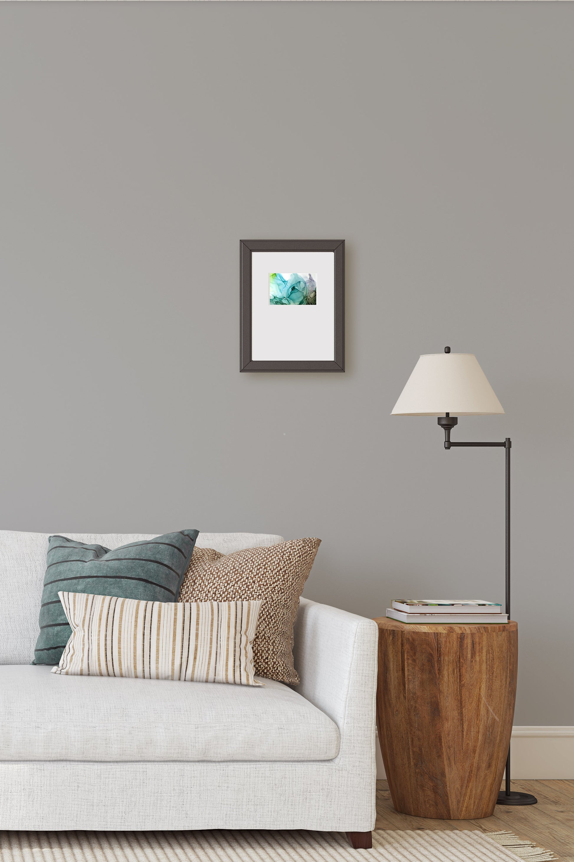 Digital mockup of the painting framed in black hung above a sofa on a light grey wall. A modern wooden end table and floor lamp sit off to the side.