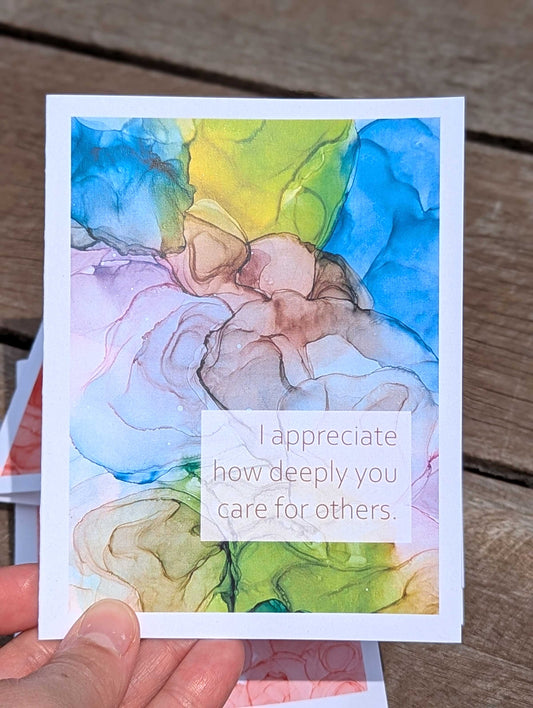 Colorful flowy ink art card with a message held above a wooden surface.