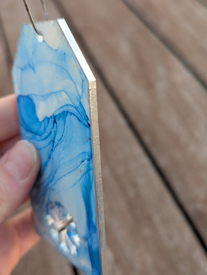 silver metallic painted edge of snowflake tag handle held by a hand on a wooden surface