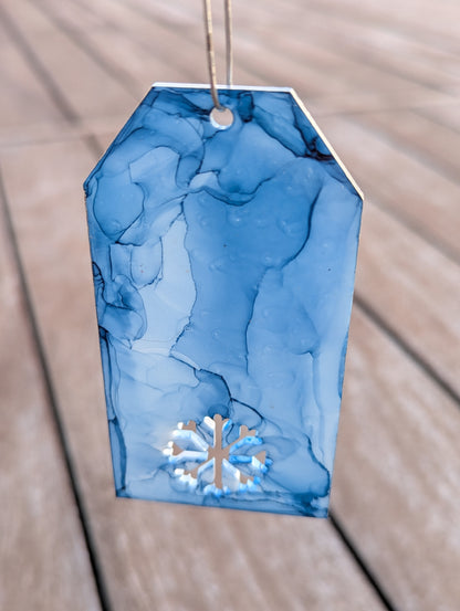 Blue marbled gift tag with a snowflake design on a wooden surface