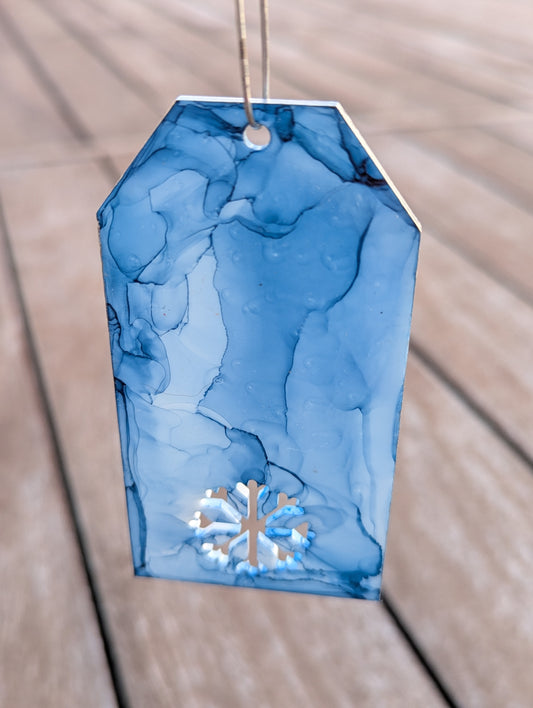 Blue marbled gift tag with a snowflake design on a wooden surface