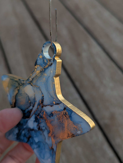 Blue and gold star ornament held by a hand against a wooden background