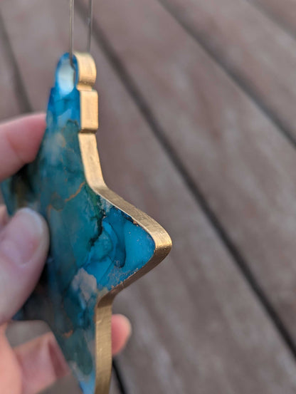 Star shaped ornament with green and gold design held by a hand on a wooden surface