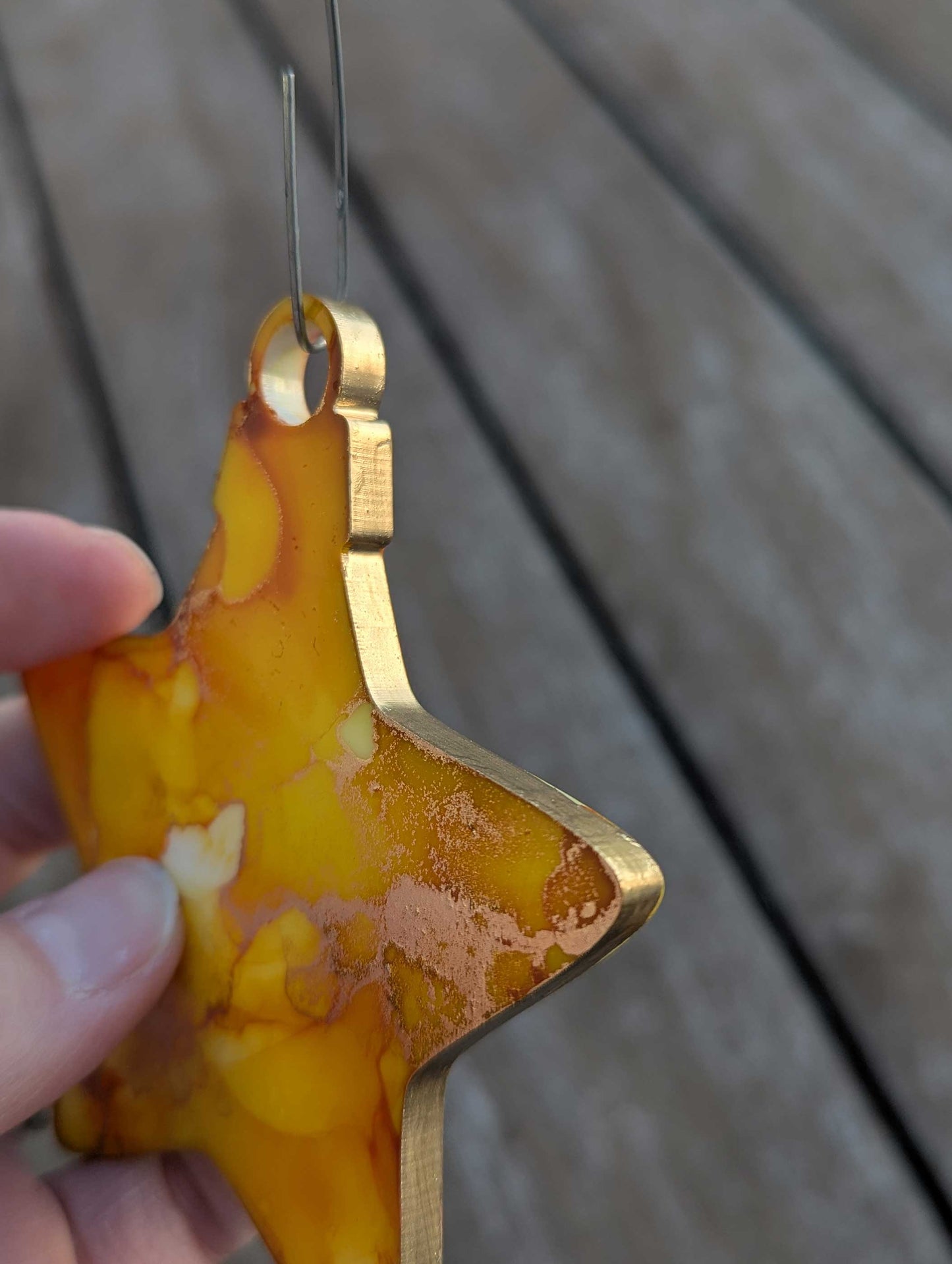 Star-shaped object with gold edge and marbled yellow surface held by a hand against a wooden background