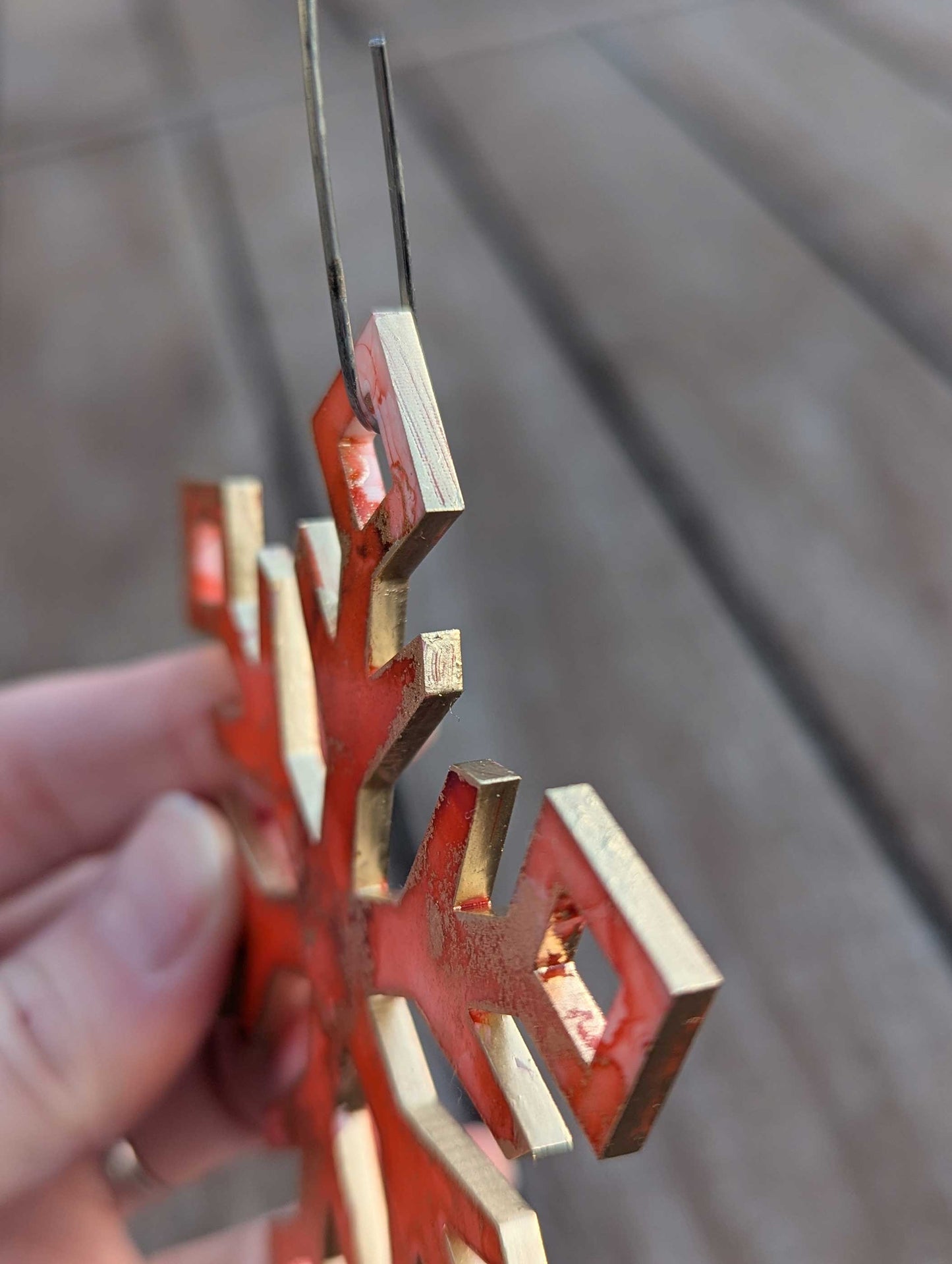 Orange/Pink  and gold snowflake ornament held by a hand against a blurred background