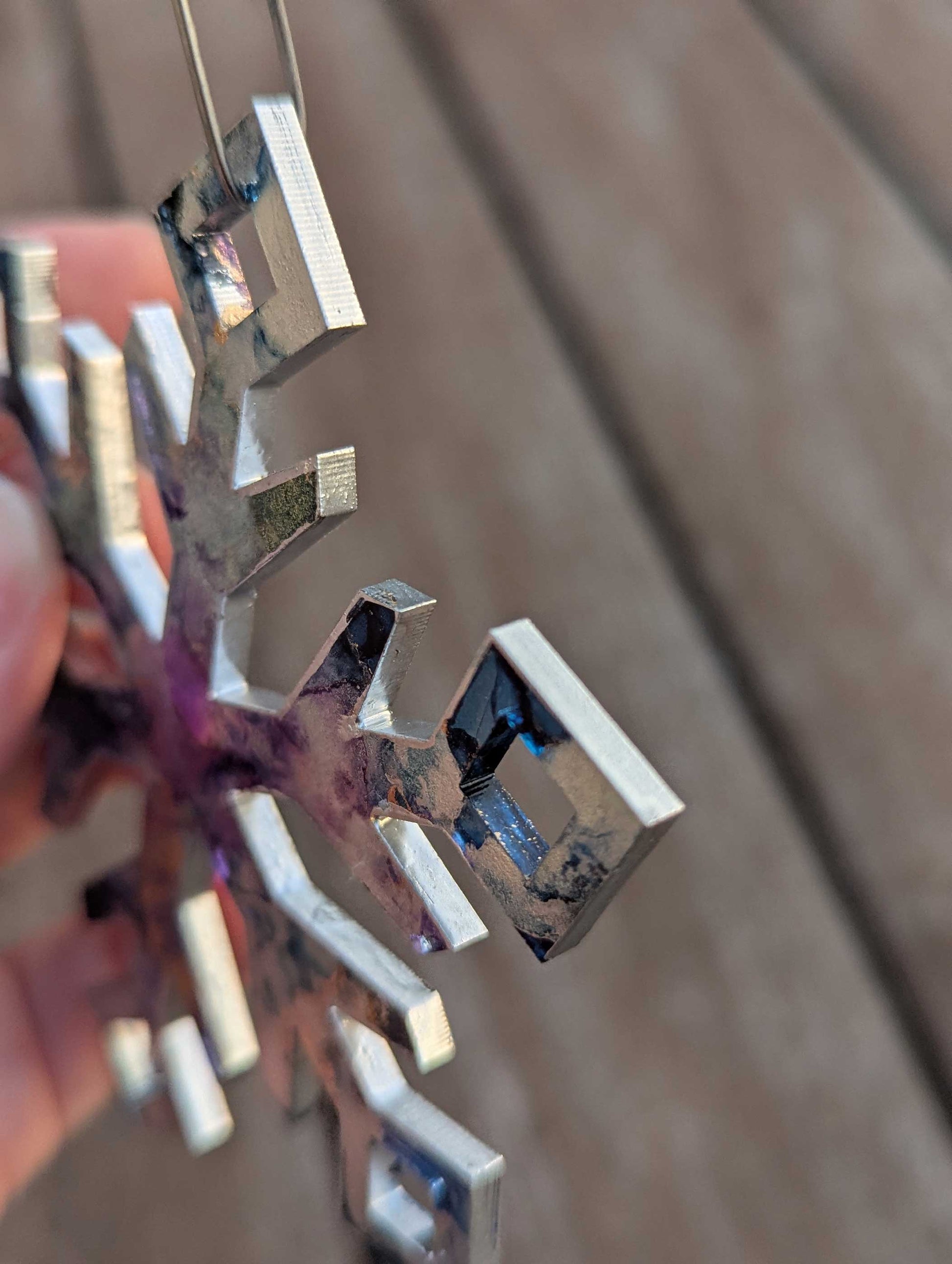 Hand painted snowflake ornament held by a hand in front of a wooden background