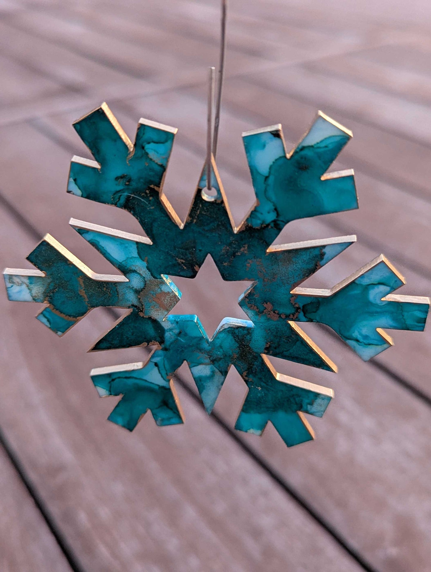 Decorative snowflake ornament with teal and gold colors on a wooden surface