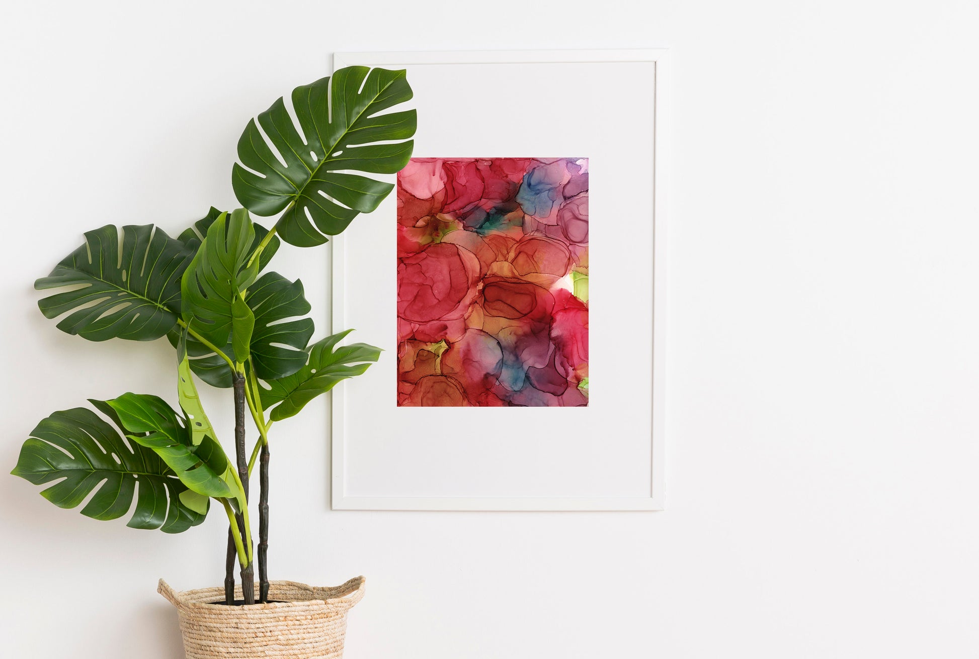 Digital mockup of A Day of Happiness framed in white hanging on a white wall. A tropical plant potted in a woven basket sits to the side.