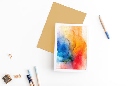 Greeting card, seen from above, with a colored, square flap envelope, pencils, pencil sharpener and shavings on a white background.