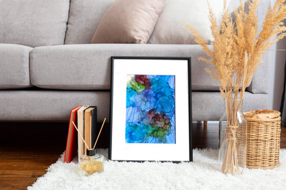 Digital mockup of Balancing Ease and Effort framed in black leaning on a white rug against the base of a light grey sofa.  Books, incense sticks, a woven basket, and dried plants in a clear vase accessorize the space.