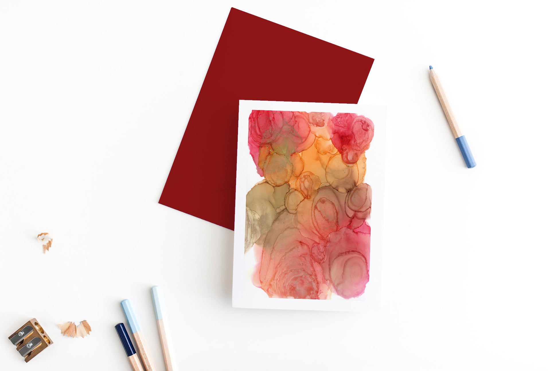 Greeting card and colorful envelope, seen from above, held by two hands along with a pencil, ready to write, against a white comforter.