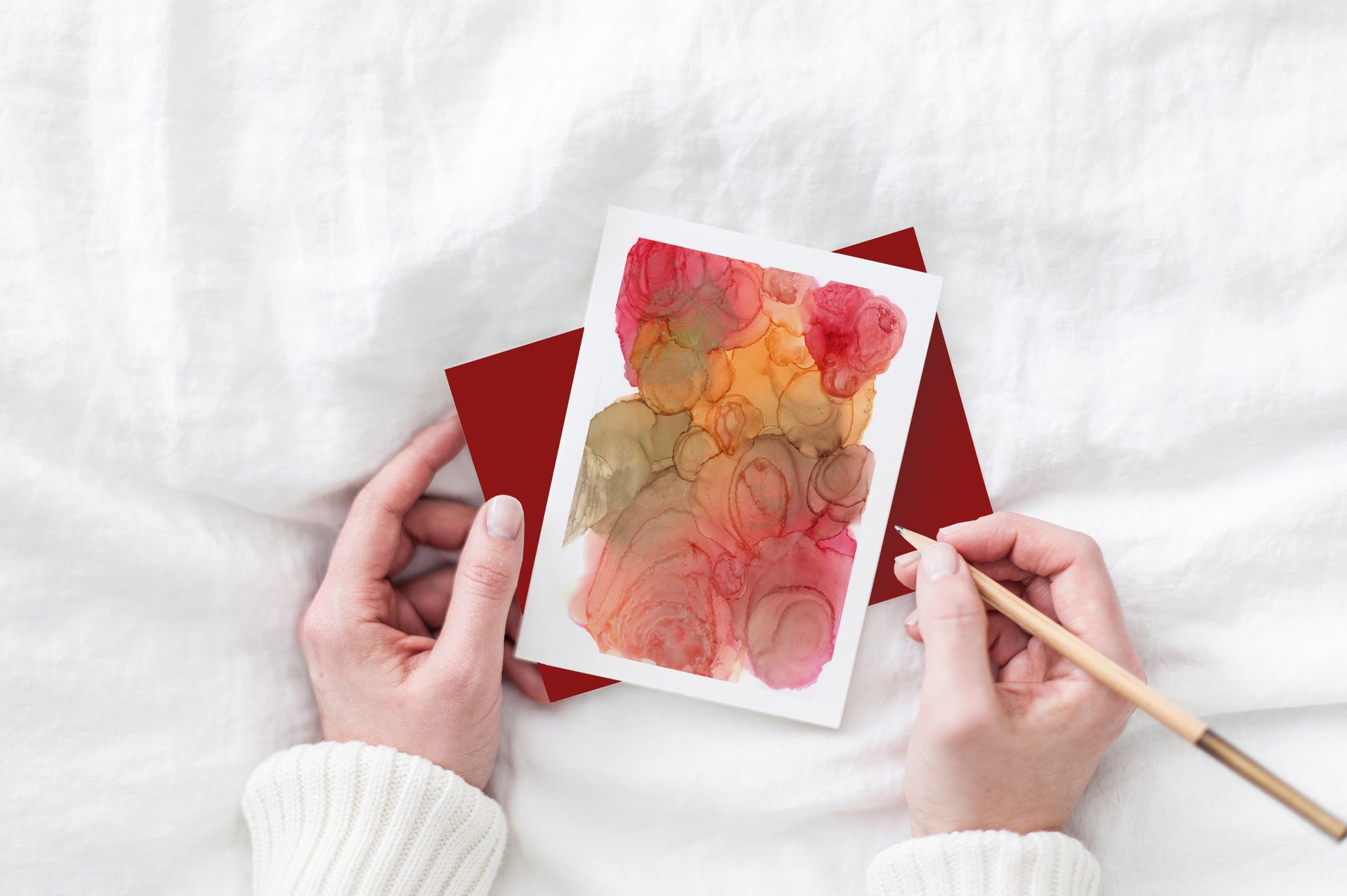 Greeting card with colorful envelope laying on a white surface with green leaves and cotton ribbon wound on wooden spools.