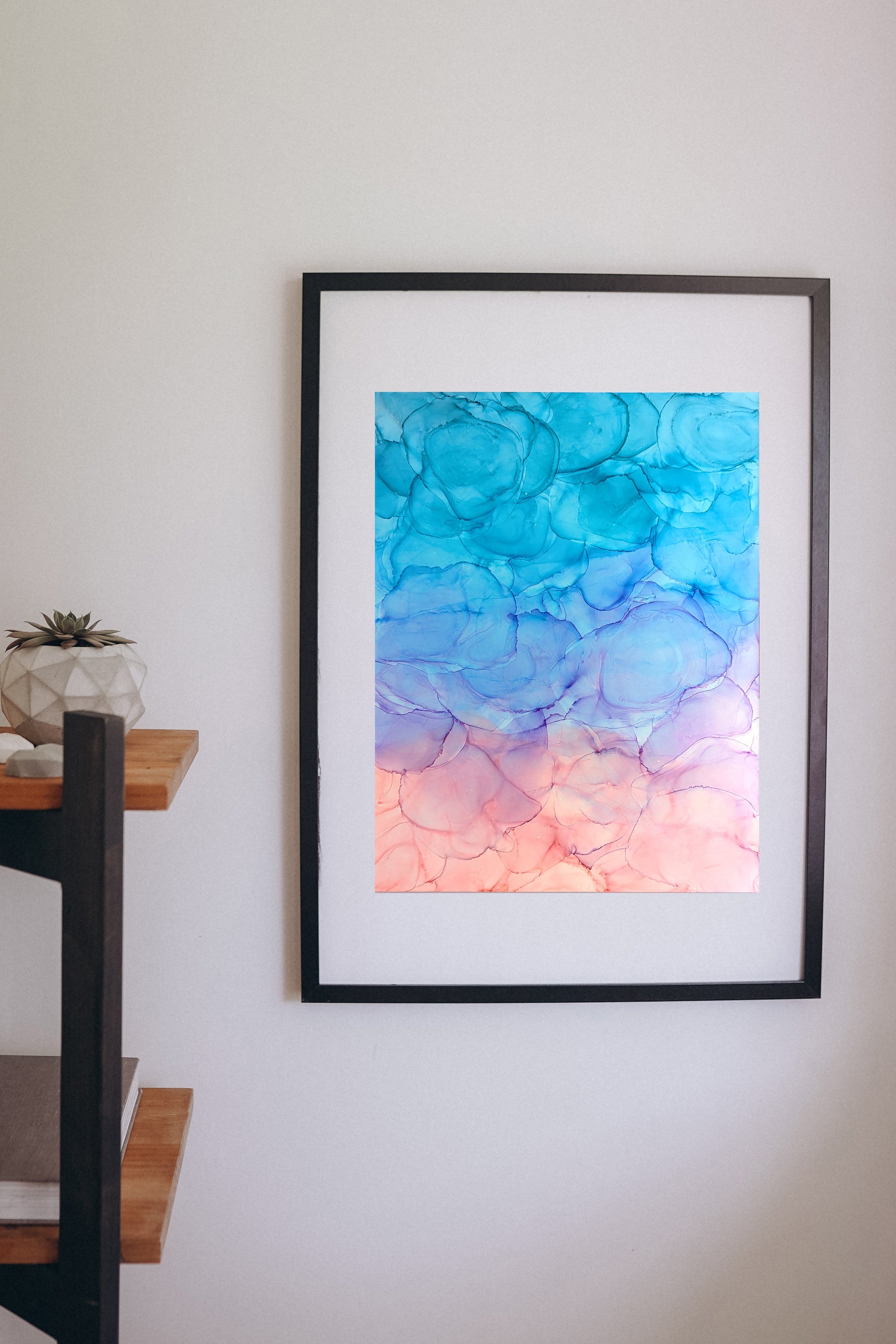 Digital mockup of Light Chaser framed in black hung on a white wall with a wooden shelf off to the side.