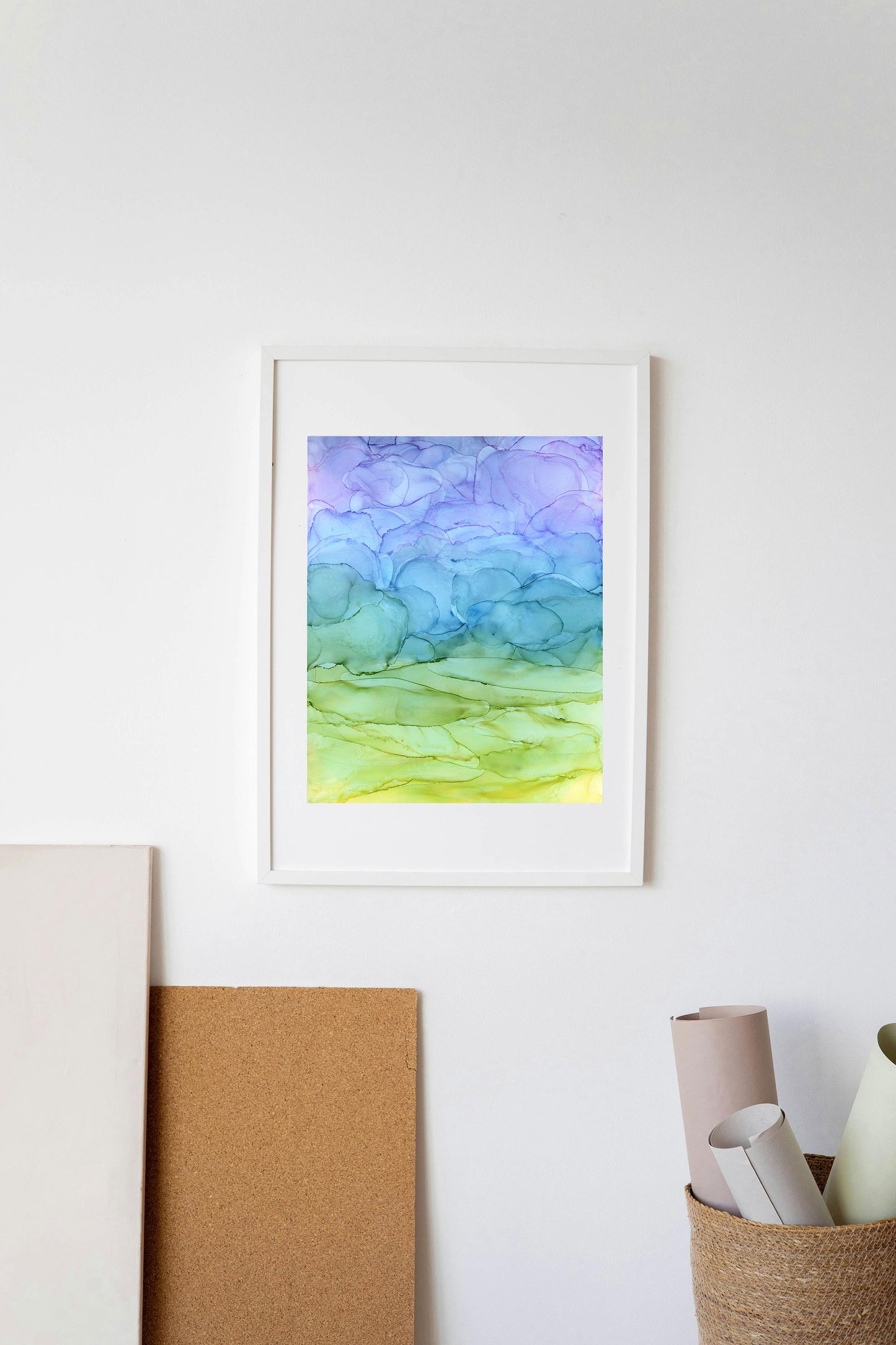 Digital mockup of Look to the Sky framed in white hung on a white wall with a basket of rolled paper and a sheet of cork below.