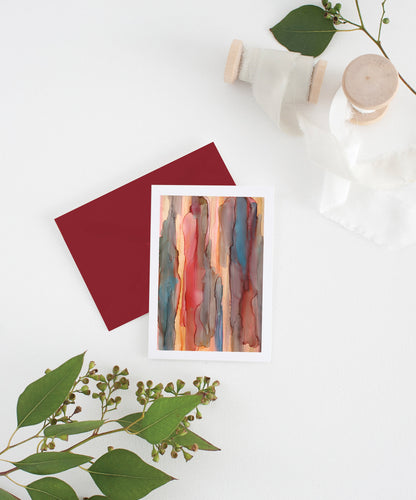 Greeting card with colorful envelope laying on a white surface with green leaves and cotton ribbon wound on wooden spools.