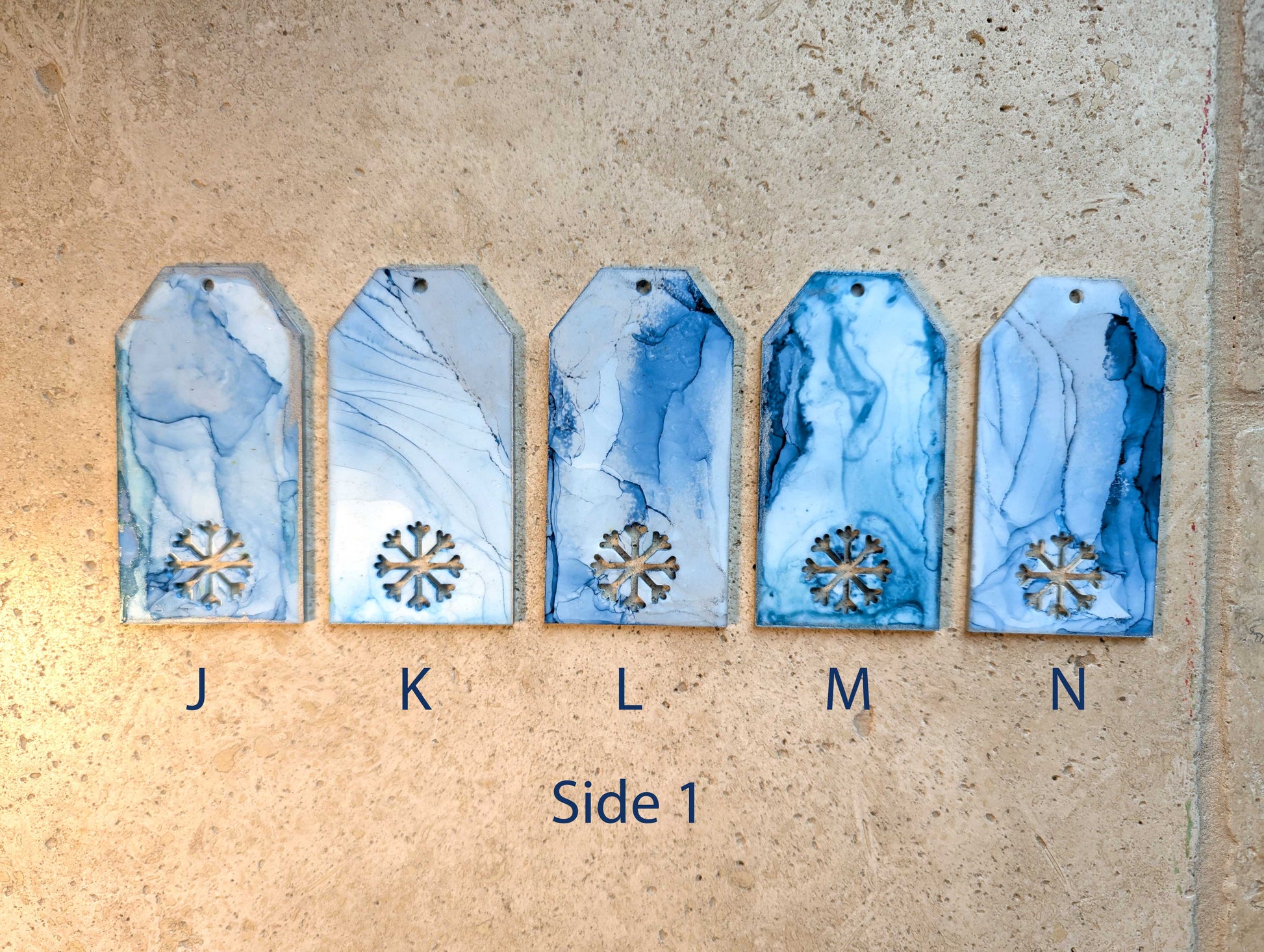 Five blue marbled tags with snowflake cutouts on a beige surface