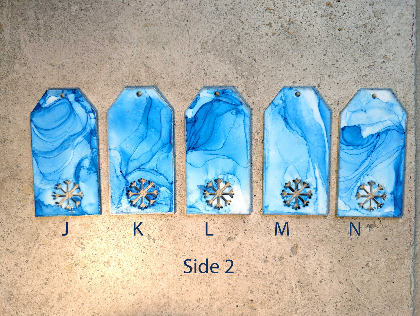 Five blue marbled tags with snowflake designs on a beige surface