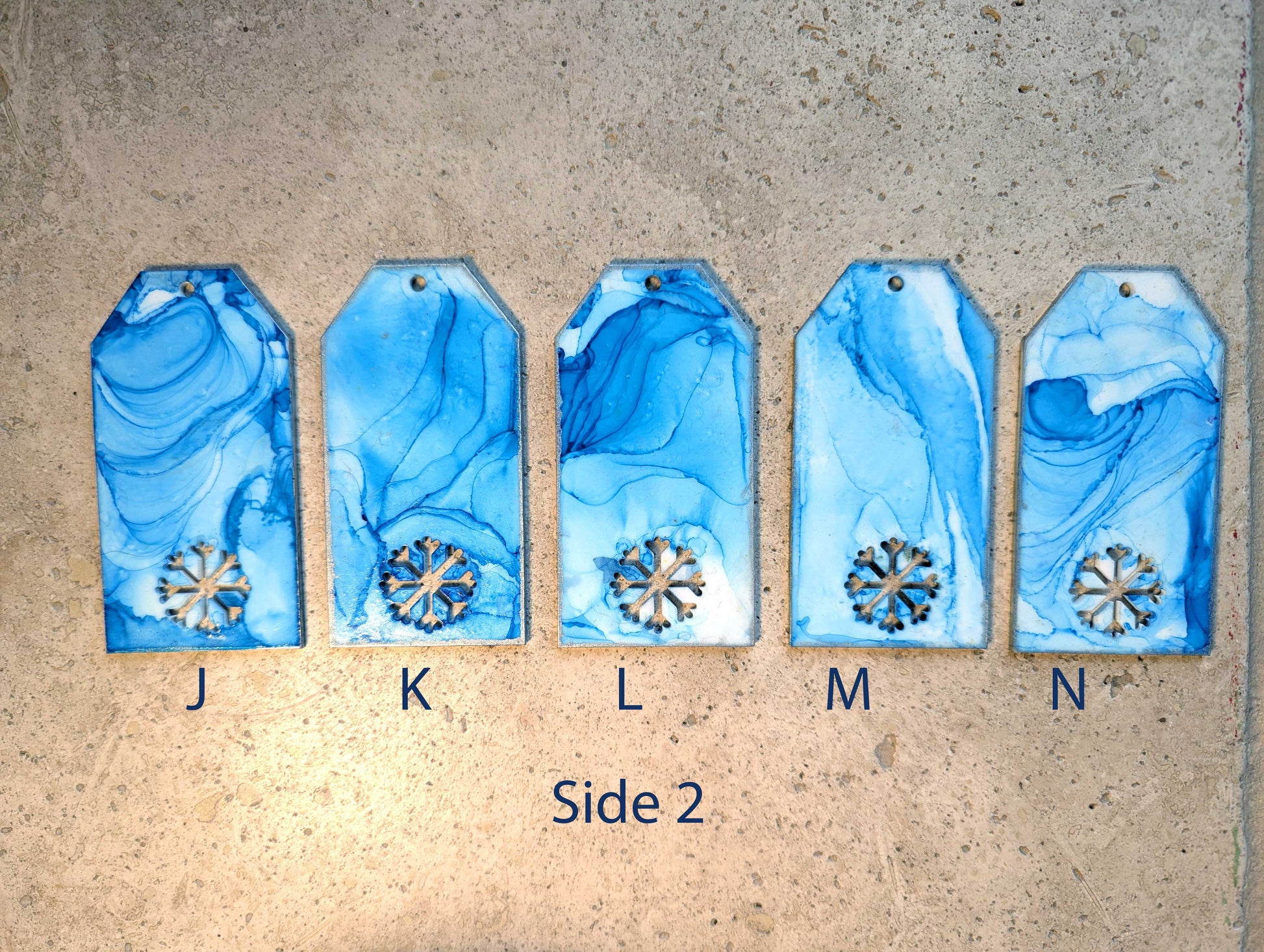 Five blue marbled tags with snowflake designs on a beige surface