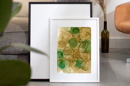 Digital mockup of Spirit of Spring framed in white on a grey tile floor leaning against a black frame and grey sofa.  A glass vase with dried stems sits to the side.